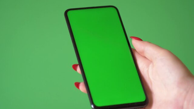 Woman hand holding the smartphone on green screen chroma key background. Mobile phone mock-up for your product. The iPhone Xr model in vertical orientation portrait mode