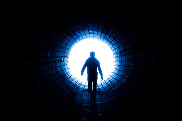 Silhouette of a man walking to the light at the end of a big tunnel. Concept of escape, exit, freedom, clinical death