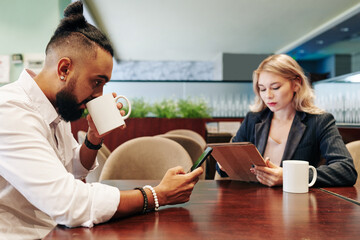 Business people drinking coffee and reading news oniline via smartphone and tablet computer when spending break in office cafe