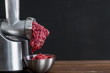 Minced meat comes out of a meat grinder on a dark background, minced meat falls into an iron plate