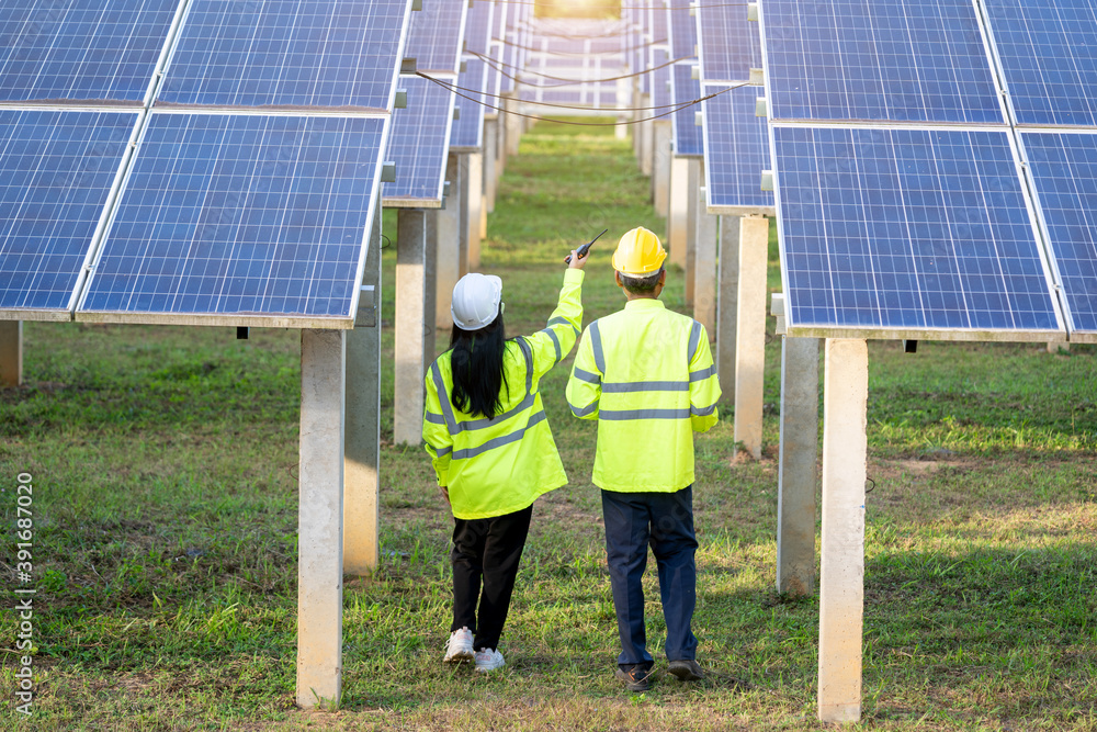 Poster two electrician workers in reflective vests and hard hats working at solar panels and talking about 