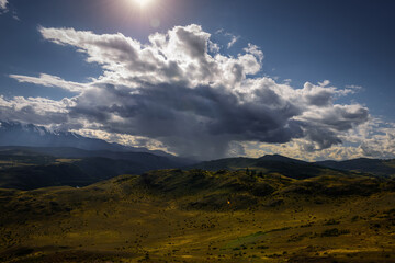 Mysterious mountain landscape with storm clouds hills and sun rays. Beautiful sky. Green grass on hills shimmers in the sunlight. Photo with tinting. Wallpaper for desktop or smartphone.