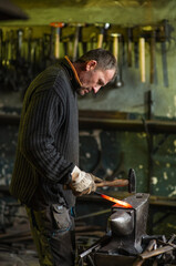 A blacksmith forging a red-hot iron billet on an anvil with a hammer. Handicraft concept