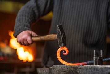 A close-up image of a blacksmith's hands forging a spiral from a red-hot billet against the background of a forge. Handicraft concept