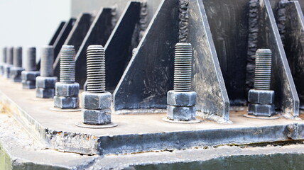 Bolts and nuts on the cement base. Several gray double bolts are firmly fixed to a steel column to...
