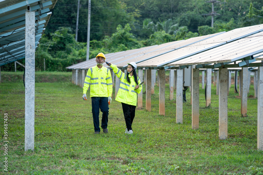 Poster two electrician workers in reflective vests and hard hats working at solar panels and talking about 