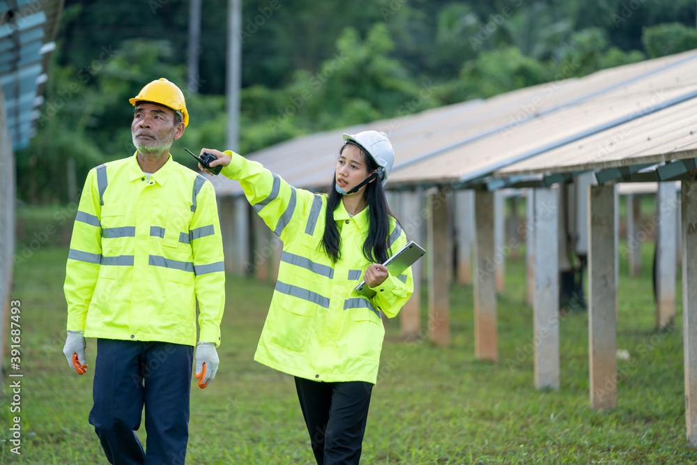 Poster Technician working with engineer planning new ecology project around field of solar panels.