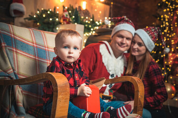 Fototapeta na wymiar Long-awaited child. Kid is sitting on the rocking chair and looking at the camera. Happy family. Christmas tree and new year decorations.
