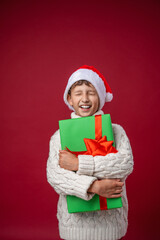 happy boy in a Santa hat holds a Christmas gift and closes his eyes