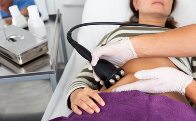 Closeup of female abdomen during professional ultrasonic fat cavitation procedure in cosmetology clinic