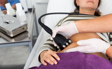 Naklejka premium Closeup of female abdomen during professional ultrasonic fat cavitation procedure in cosmetology clinic