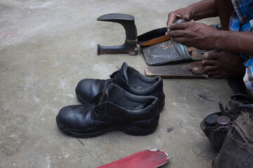 Indian local cobbler repairing shoes beside road by hand using tools in traditional way.