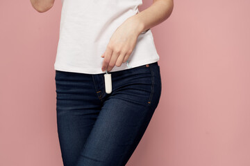 Woman with a tampon in her hand critical days hygiene white t-shirt jeans pink background menstrual cycle