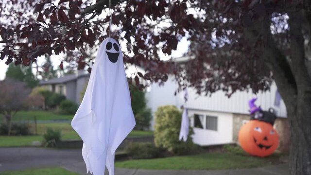 Still shot of a creepy Halloween ghost decoration hanging on a tree and swaying with the wind in a residential neighborhood.