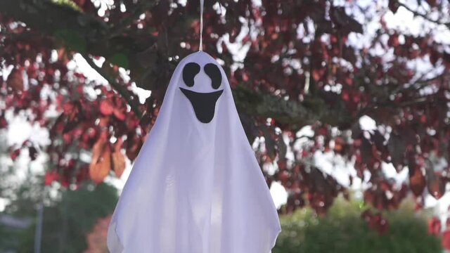 Close up tracking shot of scary Halloween ghost decoration hanging on a tree and swaying with the wind.