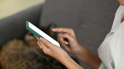Cropped shot of  woman using mobile phone with white screen while sitting on sofa at her modern home.