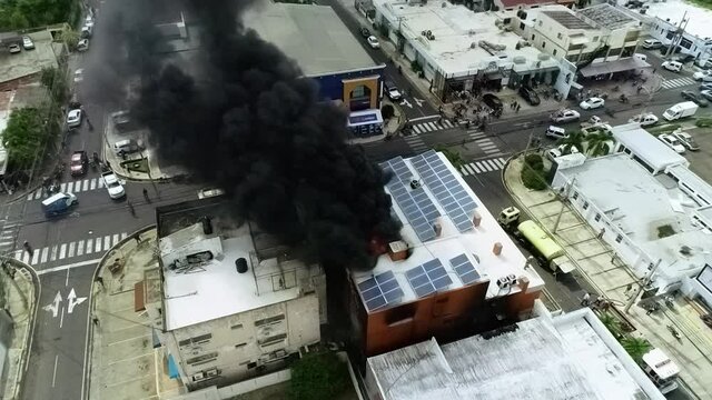 Aerial view of a building on fire, due to a explosion, dark smoke rising, in Haiti - static, drone view