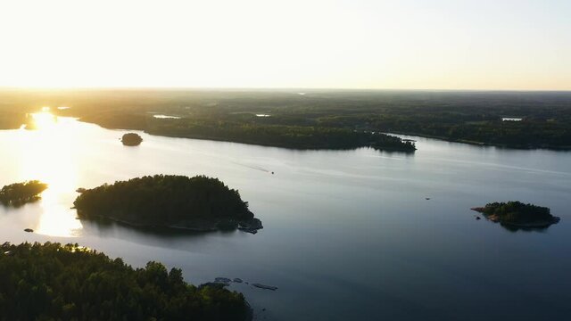 Aerial view of a boat, driving in middle of islands, colorful, summer sunset, in the archipelago, Baltic sea, in Scandinavia - tracking, drone shot