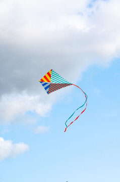 Multi-colored kite on a blue sky background with white clouds. Symbol of peace, freedom and serenity. copy cpase, place for text.
