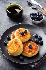 Fritters of cottage cheese with blueberries. Cheese curd cheesecakes, pancakes on a dark concrete background. Copy space.