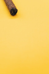 Vertical shot of a burning cigar on a yellow surface
