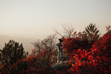 Young beautiful girl with hat standing on the top of the colourful autumn hill on sunset. Soft sunny colours.  Autumn nature. Copy space.