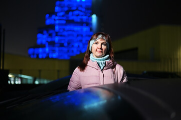 Photo of a woman in the city lights at night. The model stands directly in front of the camera against the background of city traffic.