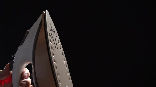 The iron is releasing steam on a black background. Close-up. Household electrical appliances concept.