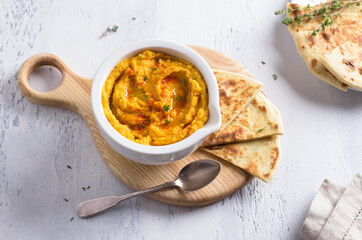 Delicious healthy homemade bean hummus with baked pumpkin, tahina and spices with flat bread on a light blue background, flat lay