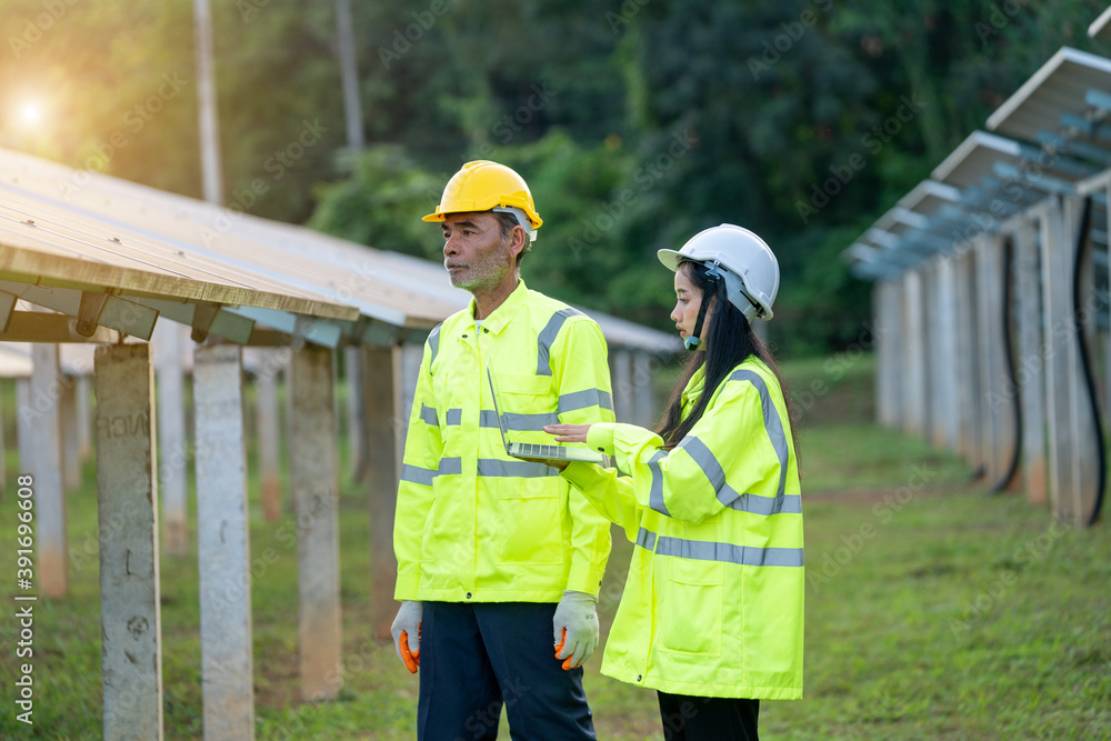 Poster two electrician workers in reflective vests and hard hats working at solar panels and talking about 