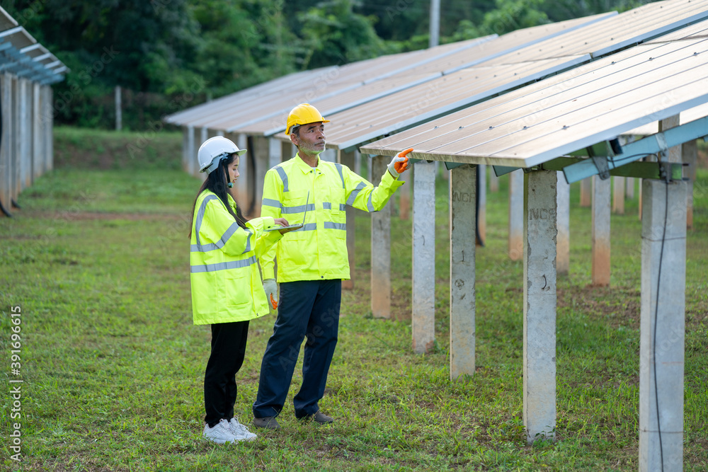 Poster Technician working with engineer planning new ecology project around field of solar panels.