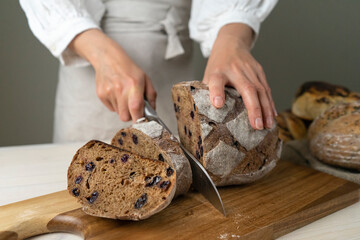  whole-grain bread put on a kitchen wooden Board with the chef holding a cutting knife. Fresh bread on the table close-up. The traditional concept of a bakery and eating healthy