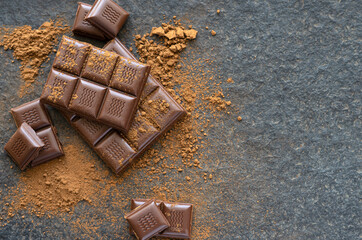 Broken pieces of chocolate and cocoa powder on a wooden background