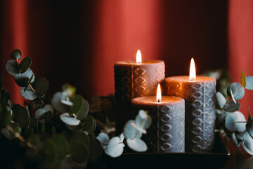 Black burning candles against dark red background with eucalyptus branch.