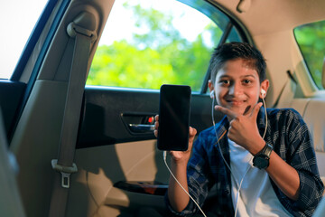Cute indian child sitting in car and showing smart phone screen with copy space