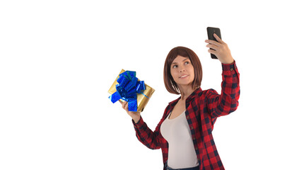 Happy young girl with short hair in red checked shirt smiles and holds gift in yellow package with blue ribbon isolated on white background and takes selfie with it, talks on the phone online