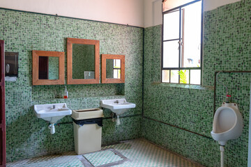 Baño antiguo público con azulejo verde y muebles blancos, eslejos de madera
