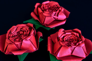 Three beautiful origami red roses with their green leaves, on a black background