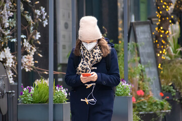 Girl wearing mask and walking in the city with smartphone at Christmas