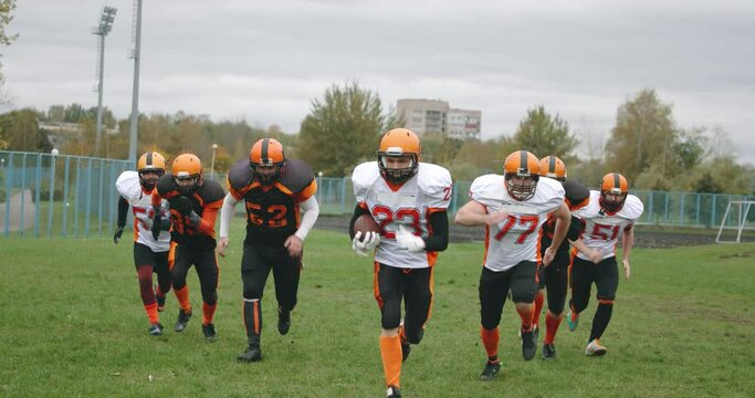 American football training day, athletic football players in protective gear run along the playing field, 4k Slow Motion.