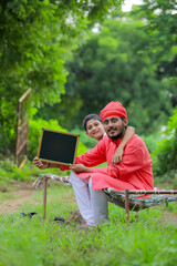 young indian farmer showing blank chalkboard with his child