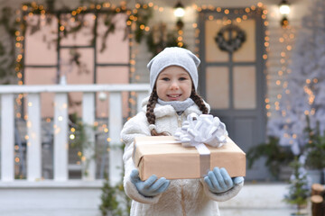Happy little girl give a gift box on the background of the Christmas house! Happy New Year and Merry Christmas!