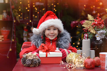 Fototapeta na wymiar Happy little girl wearing santa hat holding a gift box on the background of the Christmas background ! Happy New Year and Merry Christmas!