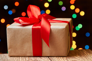 Christmas or New Year gift box with red ribbon on a wooden surface against a background of colorful...