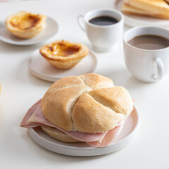 Typical Portuguese breakfast. Black coffee bica, milky coffee, bread roll with sliced cheese and ham, sandwich mixto , pastel de nata (egg tart pastry) and orange juice.