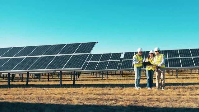 Three solar energy specialists having a discussion at a solar power plant. Drone shot