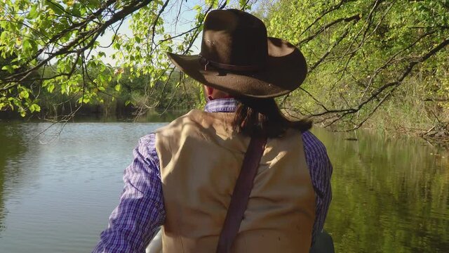 A cowboy in a canoe floats on the river in the forest. Historical reconstruction of life in the wild west of America. 4K