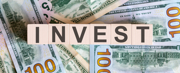 Concept words INVEST on wooden blocks on a beautiful background from dollar bills.