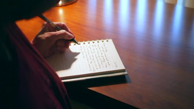 Middle aged caucasian woman with aging hands writing an old fashioned paper and pen mail letter or handwritten note to a friend on a wooden desk.