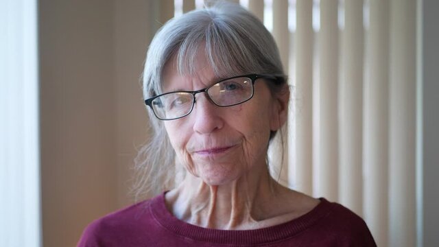 A happy old caucasian woman with aging face wrinkles gray hair and glasses looking at camera with a natural positive and optimistic outlook on life.
